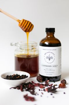 a bottle of honey sits next to a bowl of dried flowers and a wooden spoon