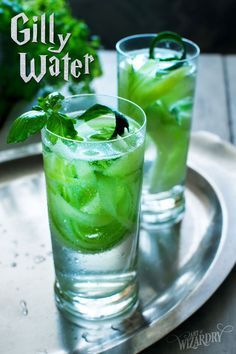 two glasses filled with ice and mint water on top of a metal tray next to lettuce