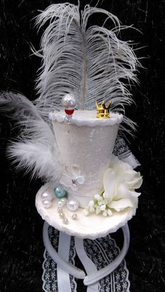 a white cake with feathers and pearls on it's top is sitting on a table