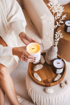 a woman is holding a candle in her hand while sitting on a couch with rocks and candles