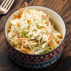 a bowl filled with coleslaw sitting on top of a wooden table next to a fork