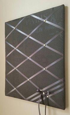 a black and silver wall hanging on the side of a wall with string attached to it