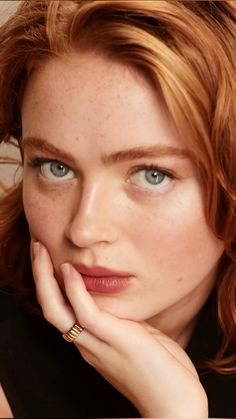 a woman with red hair and blue eyes is looking at the camera while she has her hand on her chin