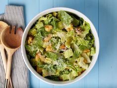 a salad with lettuce and croutons in a white bowl next to wooden spoons