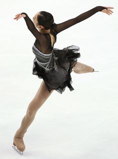 a female figure skating on the ice in a black leotard and tutu skirt