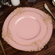 a pink plate with gold trim sits on a wooden table next to other plates and utensils