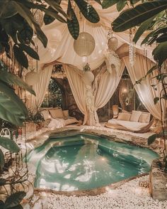 an indoor pool surrounded by greenery and hanging lights with curtains on the ceiling above it