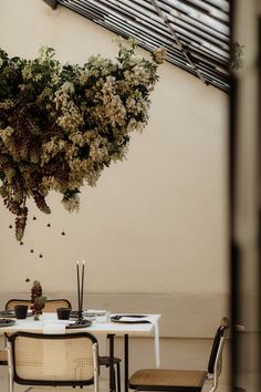 a dining room table with chairs and flowers hanging from it's ceiling over it