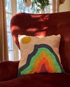 a colorful pillow sitting on top of a red chair in front of a potted plant