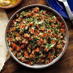 a bowl filled with lots of food next to some pita bread on top of a wooden table