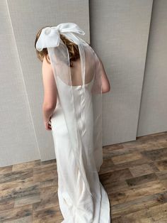 a woman in a white wedding dress is looking down at the wall with her back to the camera