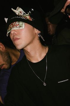 a man wearing a black hat and bandanna around his face with other people in the background