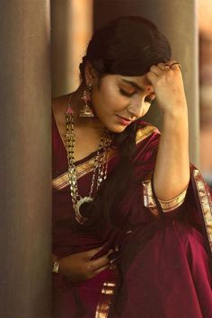 a woman in a maroon sari is leaning against a pillar with her hand on her head