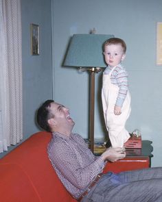 a man sitting on top of a red couch next to a baby in his arms