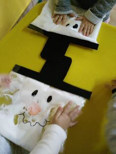 two children are making a paper snowman craft on a yellow table with black and white squares