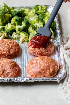 a person using a spatula to spread ketchup on meatballs and broccoli