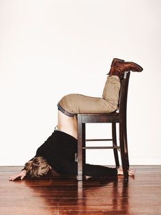 a woman laying on the floor in front of a chair with her leg up and head down