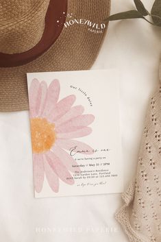 a pink flower on top of a card next to a hat