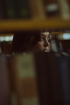 a girl looking through the bookshelves in a library at night with only one eye open