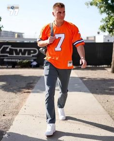 a man in an orange jersey is walking down the sidewalk