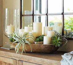 candles and succulents are arranged in a wooden bowl on a table next to a mirror