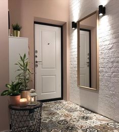 a white door with two mirrors and candles on the floor in front of it, next to a potted plant