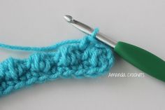 the crochet stitch is being worked on with a green handled knitting needle in front of it