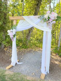 a white wedding arch with flowers and greenery on the ground in front of trees