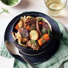 a black plate topped with meat, potatoes and carrots next to a glass of water