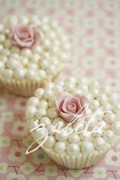 two cupcakes decorated with pink roses and pearls on a tablecloth that says sweet