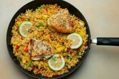 a skillet filled with chicken and rice covered in lemon wedges on top of a white table