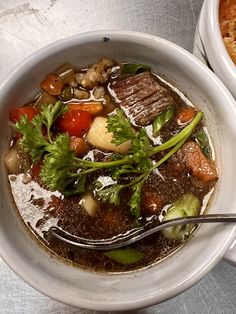 two bowls filled with soup and vegetables on top of a white table cloth next to each other