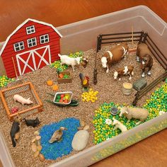 a plastic container filled with toys and farm animals on top of a wooden table next to a red barn