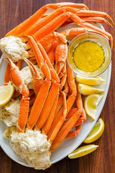 crab legs with lemon wedges and butter on a white plate next to dipping sauce