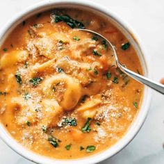 a person holding a spoon over a bowl of soup with ravioli and spinach