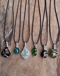 four necklaces with different designs on them sitting on top of a wooden table next to each other