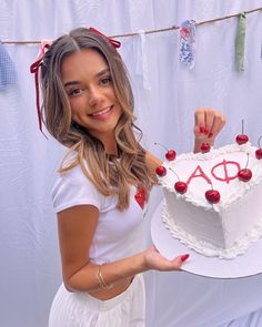 a woman holding a white cake with cherries on it and the word ao spelled in red