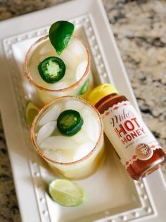 three glasses filled with drinks sitting on top of a white plate next to limes