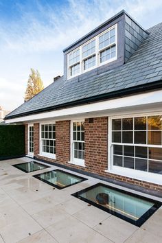 an outdoor swimming pool in front of a brick house with white windows and tiled roof