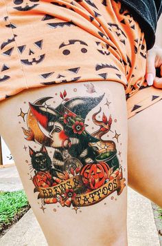 a woman's thigh with tattoos on it and an image of a cat wearing a witches hat