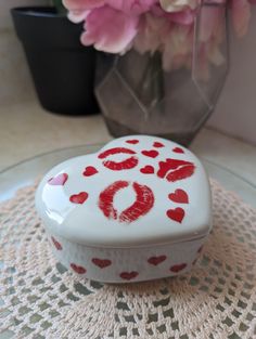 a heart shaped box with lipstick painted on it sitting on a doily next to flowers