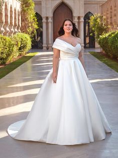 a woman in a white wedding dress standing on a walkway outside an ornate building with arches