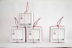 four white boxes with red string tied to them on top of a wooden table in front of a white wall