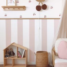 a room with pink and white striped wallpaper, wooden dollhouse shelves and a teddy bear hanging on the wall