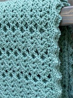 there is a green crocheted blanket hanging on the back of a wooden chair