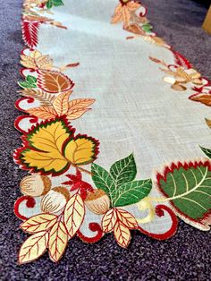 an embroidered table runner with leaves and acorns on the edge is sitting on a carpeted floor