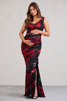 a pregnant woman wearing a black and red dress with floral print on the side, standing in front of a gray background