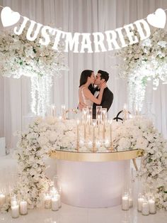 a newly married couple kissing in front of a cake with candles and flowers on it