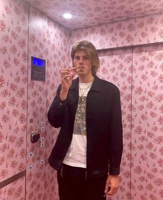 a man standing in front of a pink wall with flowers on it brushing his teeth