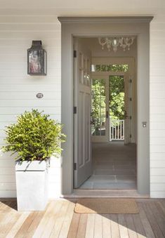 an open door leading to a white house with two plants on the front porch and another planter